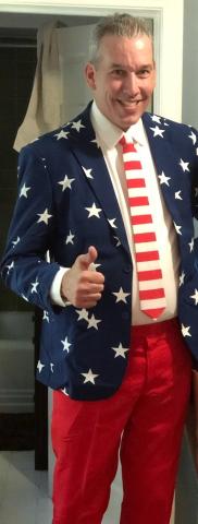 A smiling man in a blue jacket with white stars, red pants, and a red and white striped tie