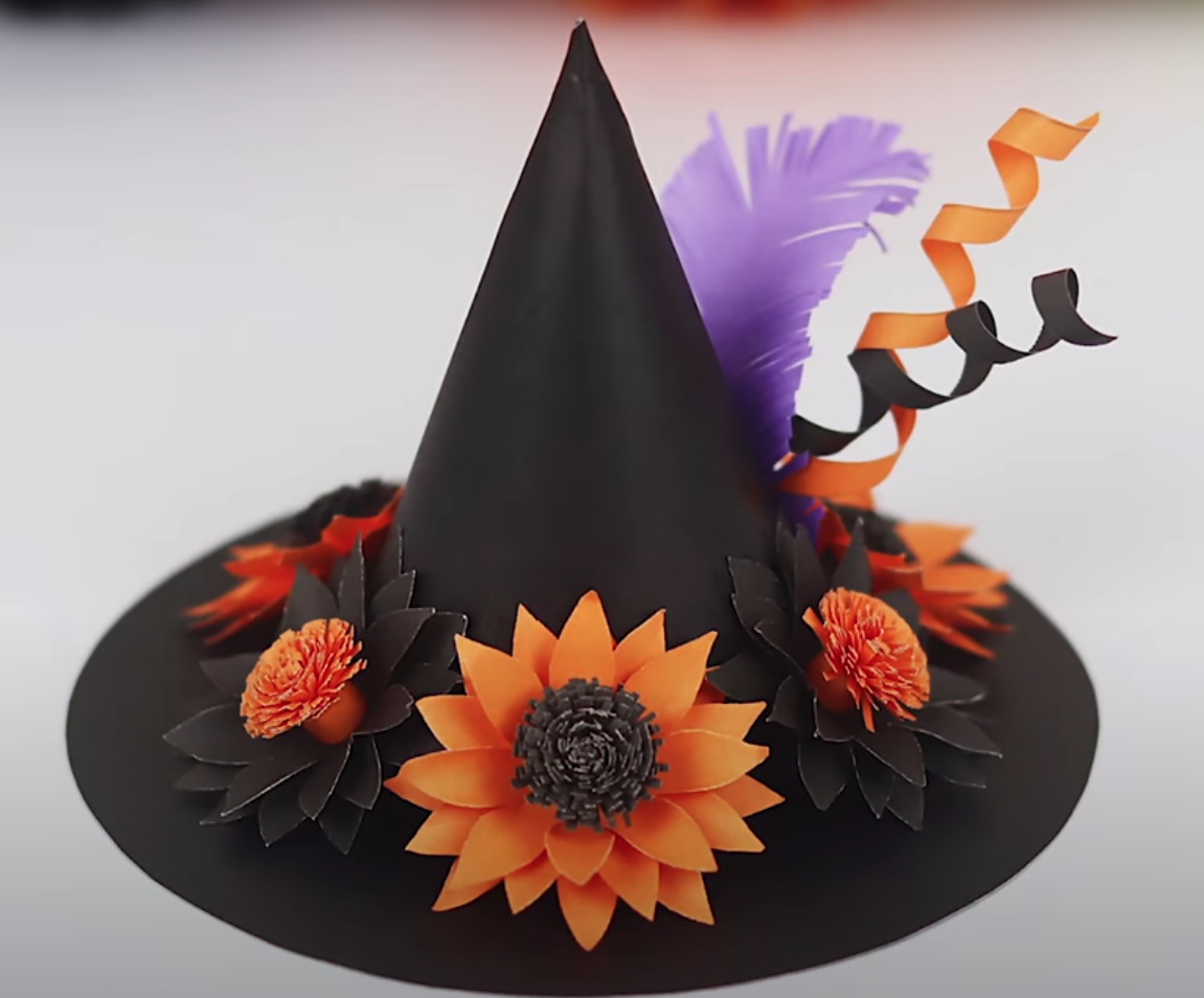 A pointed black witch hat made from paper and decorated with orange and purple flowers and feathers